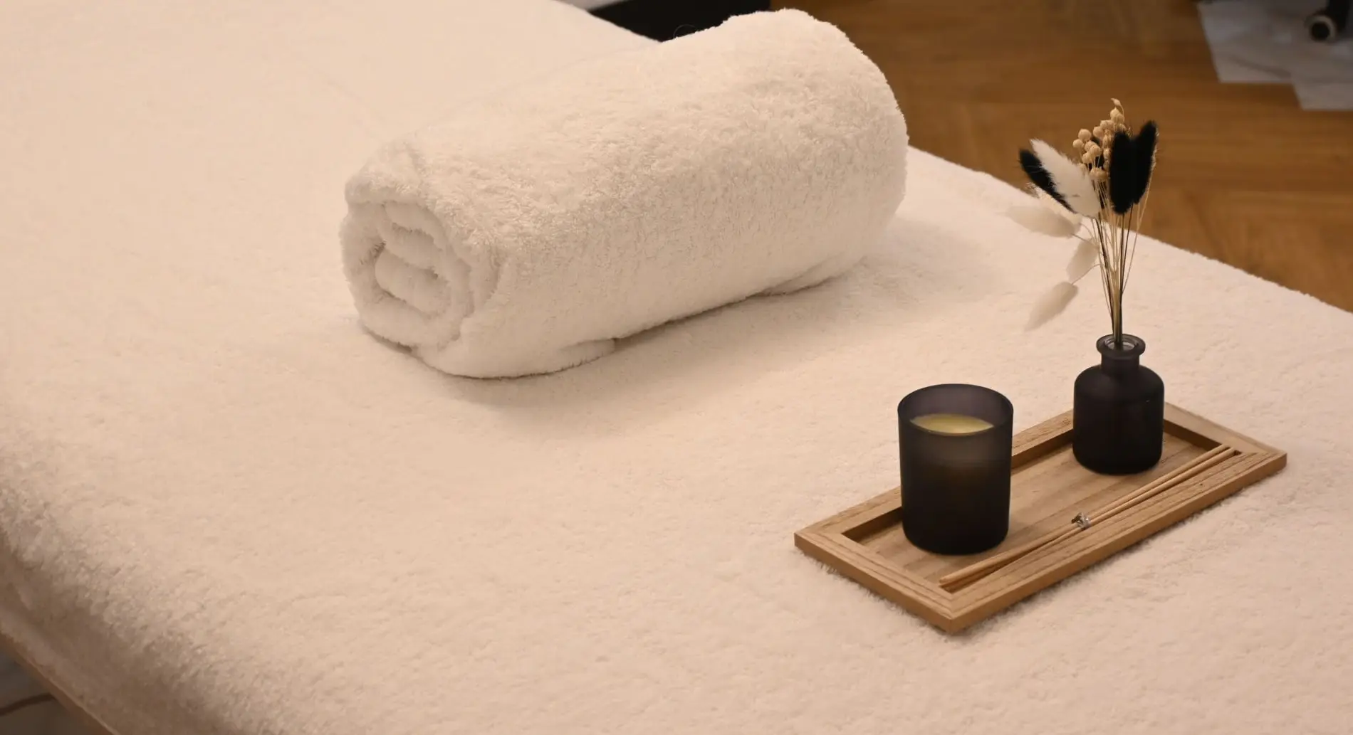 Une serviette blanche roulée, une bougie et des fleurs séchées sur une table de massage